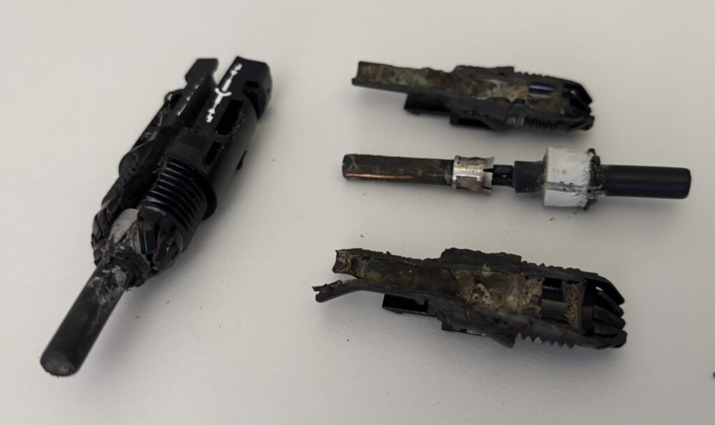 Vier stark verbrannte und deformierte DC-Steckverbinder einer Photovoltaikanlage auf weissem Untergrund. Die Kunststoffgehäuse sind geschmolzen und geschwärzt, die Metallkontakte korrodiert und teilweise freigelegt.